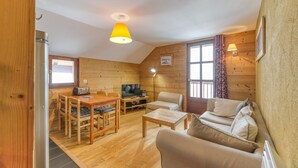 A cozy cabin interior with a wooden dining table, chairs, a sofa, a TV, and a lamp. - Apartment 'Regain 7' with Mountain View and Balcony (Villard-Reculas)