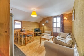 A cozy cabin interior with a wooden dining table, chairs, a sofa, a TV, and a lamp.