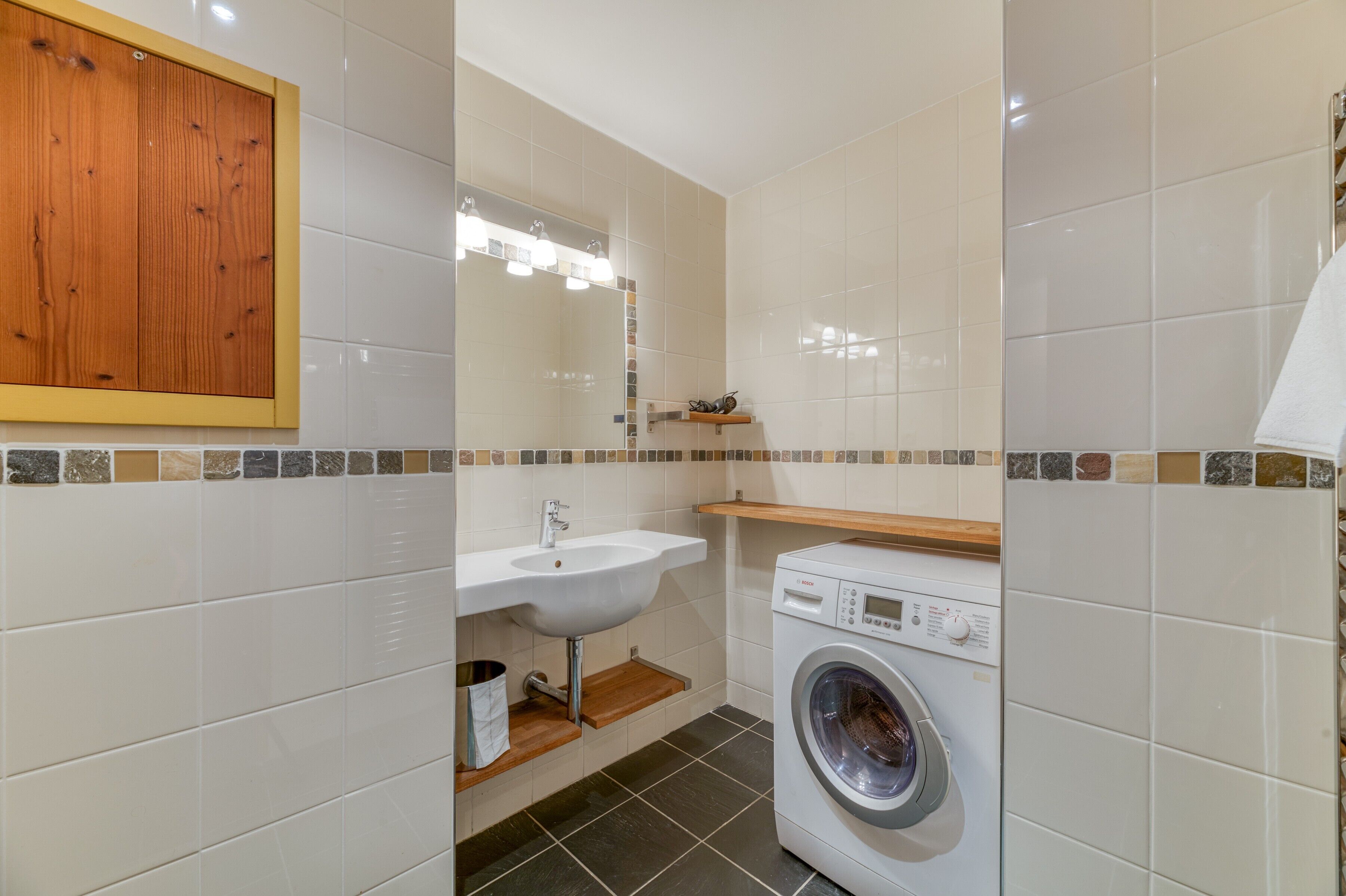 Un baño pequeño con lavabo, espejo, estante de madera y lavadora.