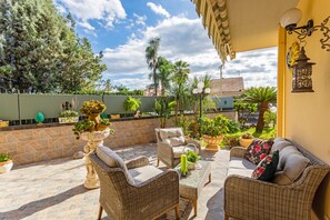 Eine Terrasse mit Korbmöbeln, Topfpflanzen und einer Steinmauer.