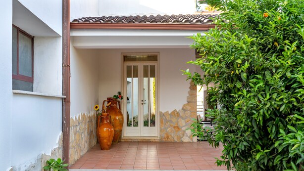 Une entrée de maison avec un porche carrelé, un mur en pierre et de grands vases.