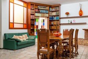 A living room with a green sofa, wooden dining table, chairs, and a bookshelf filled with books. - Villa 'Dany with Pool' with Private Pool, Wi-Fi and Air Conditioning (Villa Castelli)