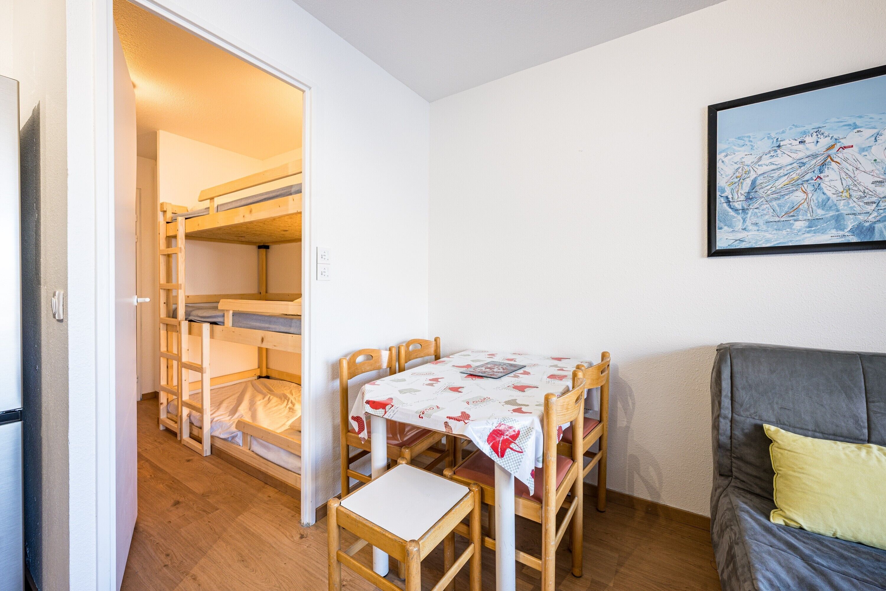 Een kamer met stapelbedden, een eettafel met stoelen, een bank en een lijst aan de muur.
