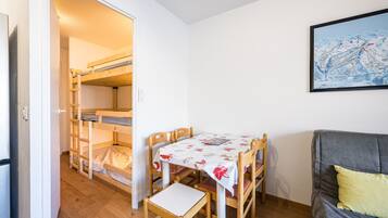 Een kamer met stapelbedden, een eettafel met stoelen, een bank en een lijst aan de muur.