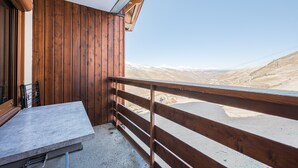 Ein Balkon mit Holzgeländer, einem Tisch und Blick auf eine gebirgige Landschaft.