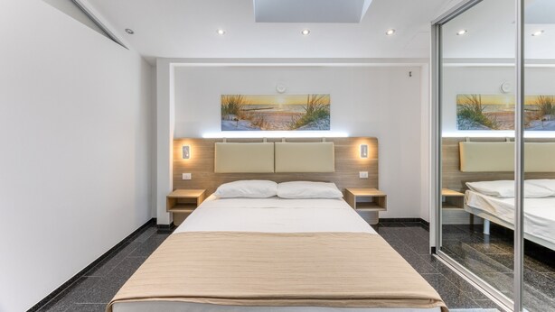 A modern hotel room with a skylight, a large bed, bedside tables, and artwork on the walls.