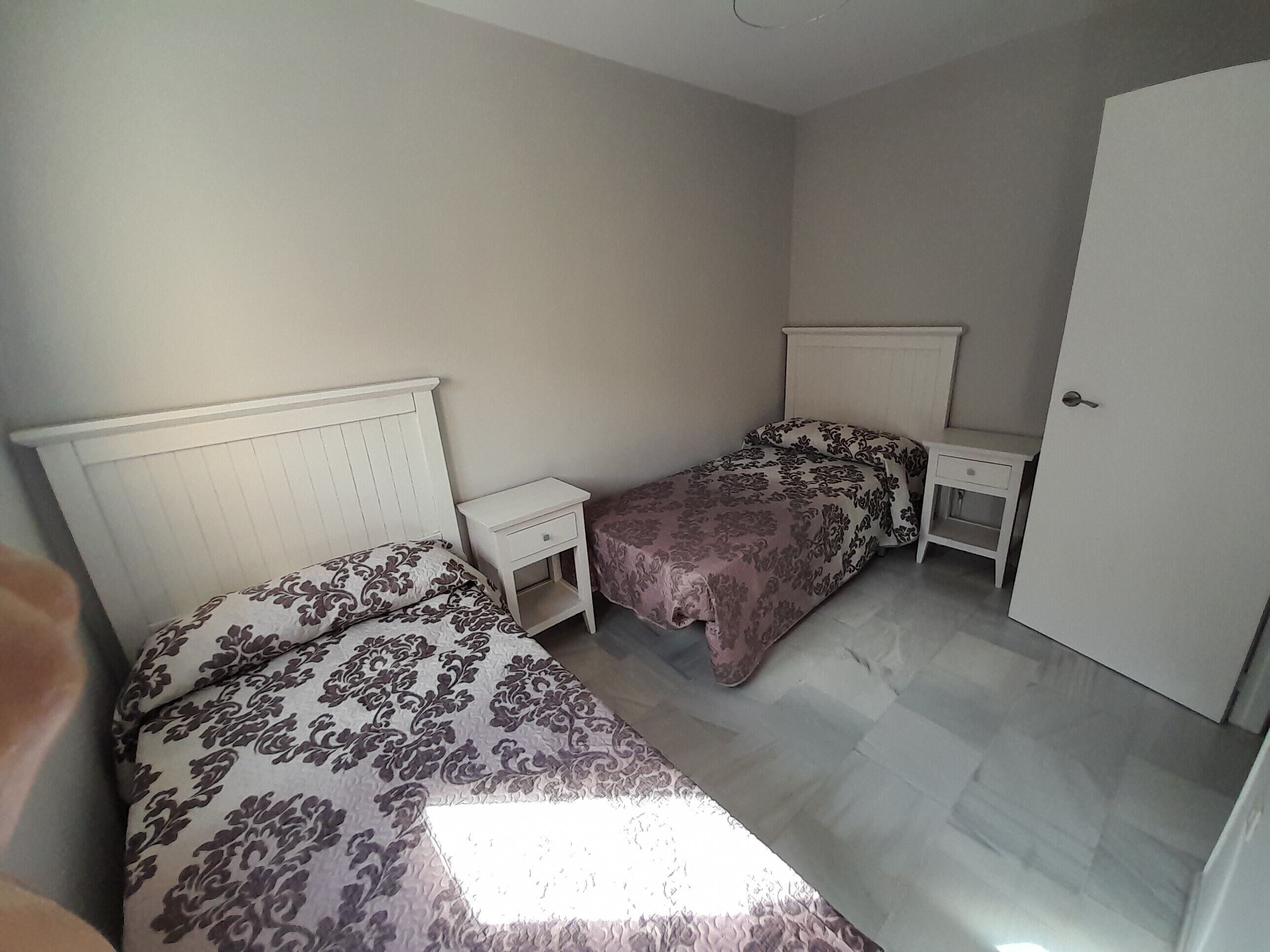 Une chambre avec deux lits, une table de chevet, une commode et une porte.