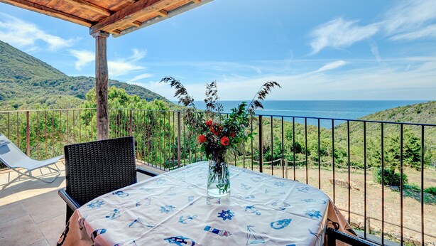Ein Balkon mit Tisch, Stuhl und Blumen in einer Vase.