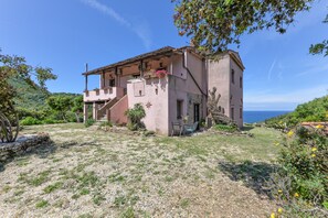 Ein zweistöckiges Haus mit Balkon, einer Steinmauer und Blick aufs Meer.