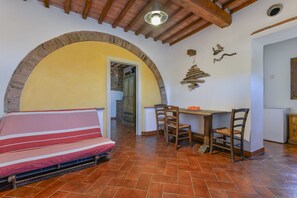 Una habitación con sofá, una mesa de comedor con sillas, una zona de cocina y un arco de ladrillo.