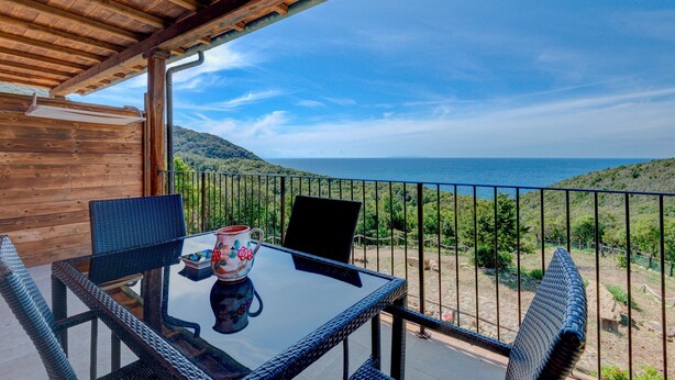 Un balcon avec une table et des chaises, offrant une vue panoramique sur la mer et les collines.