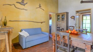 Une pièce avec un canapé bleu, une table à manger en bois avec des chaises, un meuble et des branches fixées au mur.