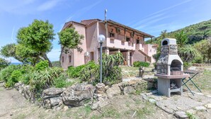 Une maison à deux étages avec une cheminée en pierre, un mur en pierre et une vue sur la mer.