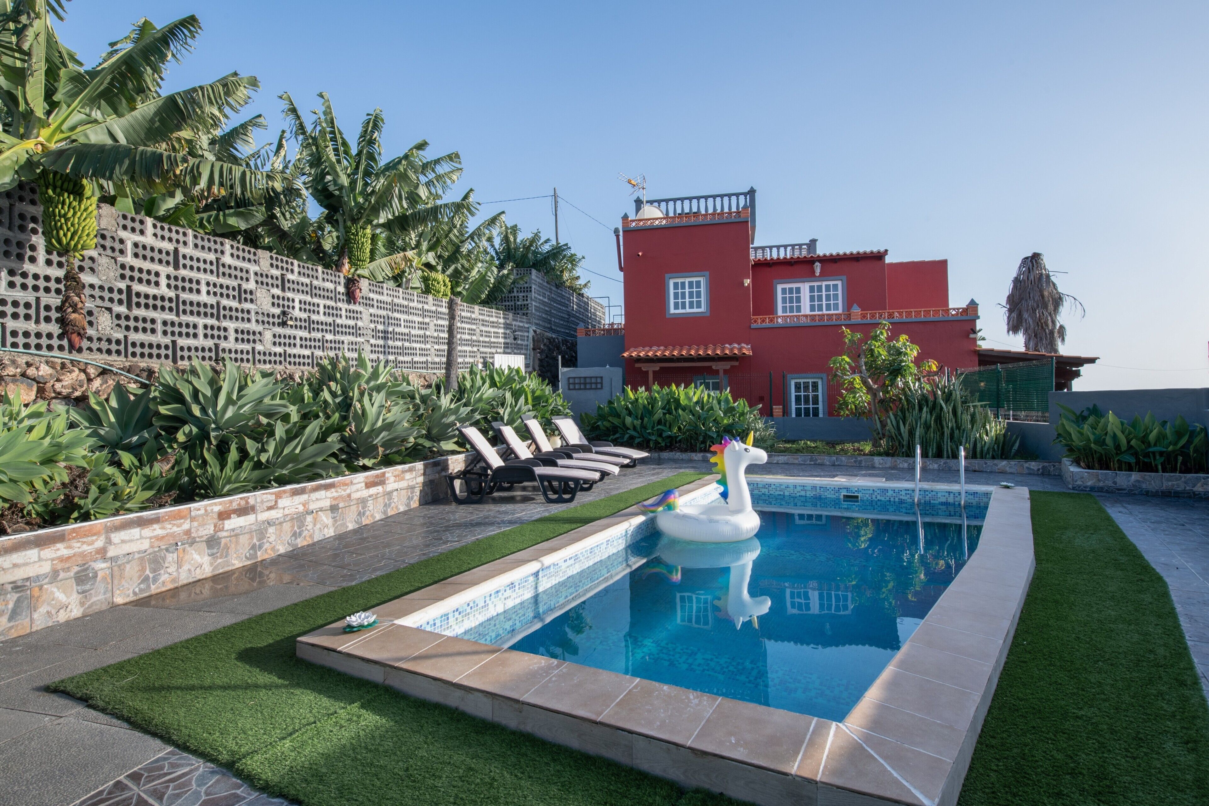 A swimming pool with a swan float, surrounded by a well-maintained lawn and a red building in the background.