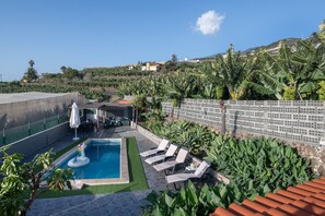 A swimming pool with lounge chairs, a small play area, and a view of a hillside with vegetation. - Rural House 'Los Lilos' with Private Pool, Private Garden, and Wi-Fi (Tijarafe)
