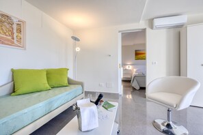 Ein modernes Zimmer mit einer Couch, einem weißen Sessel, einem Tisch mit Flasche und Gläsern sowie einem Bild an der Wand.