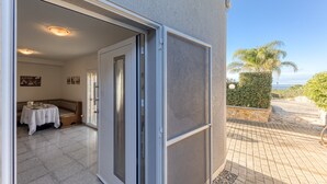 An open sliding door leading to a room with a table and a bench, a tiled floor, and a view of the outdoors.