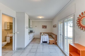 Huoneessa on pieni keittiönurkkaus, ruokailutila, jossa on pöytä ja penkki, suuri ikkuna, josta on näkymä, sekä aurinkoa kuvaava koriste seinällä.