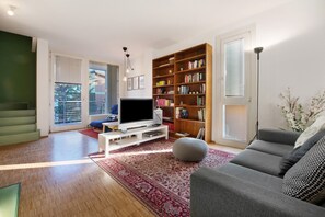 Un salon avec un téléviseur à écran plat, une bibliothèque, un canapé gris et un tapis rouge à motifs.