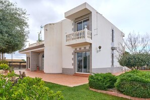 Una casa moderna de dos pisos con balcón, patio cubierto y jardín bien cuidado.