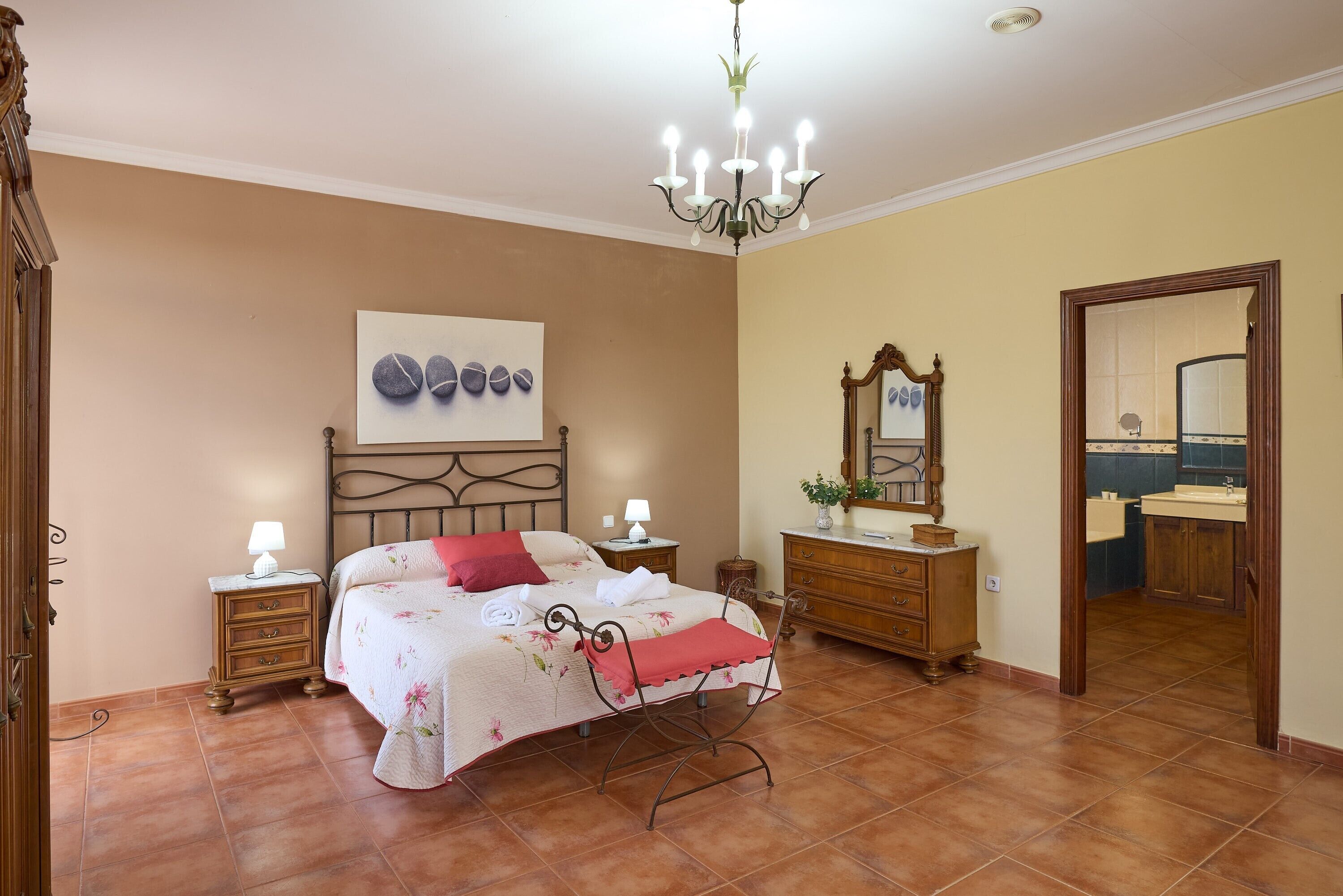 A bedroom with a bed, bedside tables, a dresser, a mirror, and a chandelier.