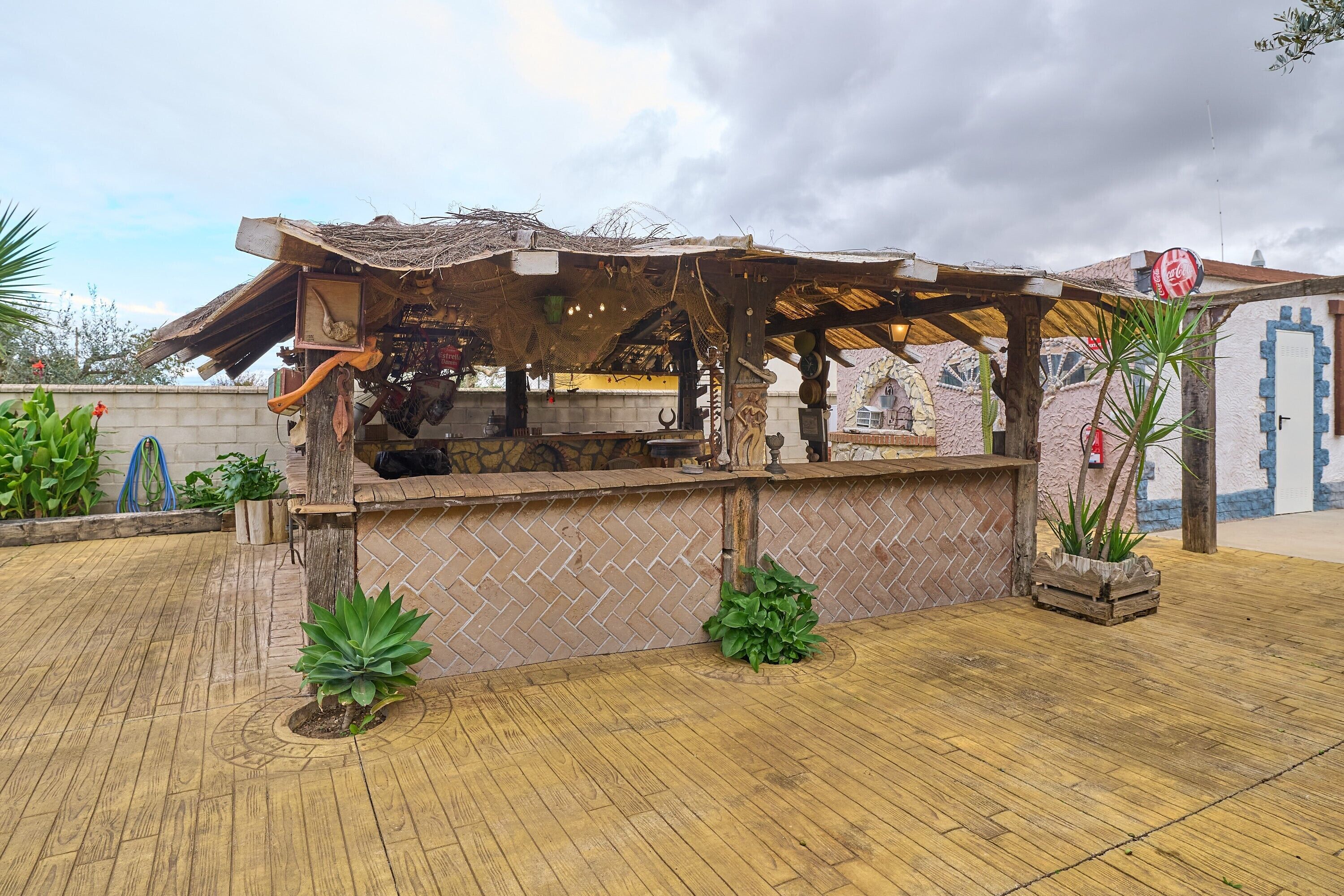 A rustic outdoor bar with a wooden structure, a Coca-Cola sign, and potted plants.