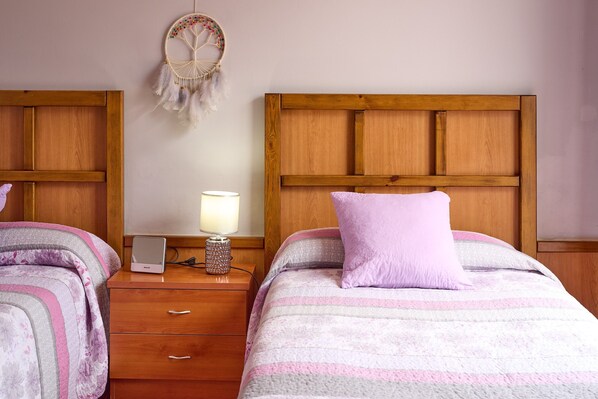 A bedroom with two beds, wooden headboards, a bedside table with a lamp, and a dreamcatcher on the wall.