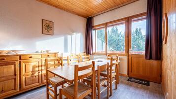Comedor de madera con mesa y sillas, cocina con armarios de madera y ventanas grandes con cortinas.