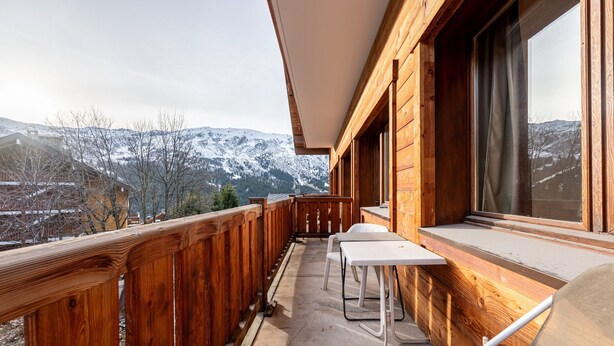 A wooden balcony with a view of snow-capped mountains, a table, and chairs. - Apartment 26 – 9 Guests with Mountain View and Balcony (Les Allues)