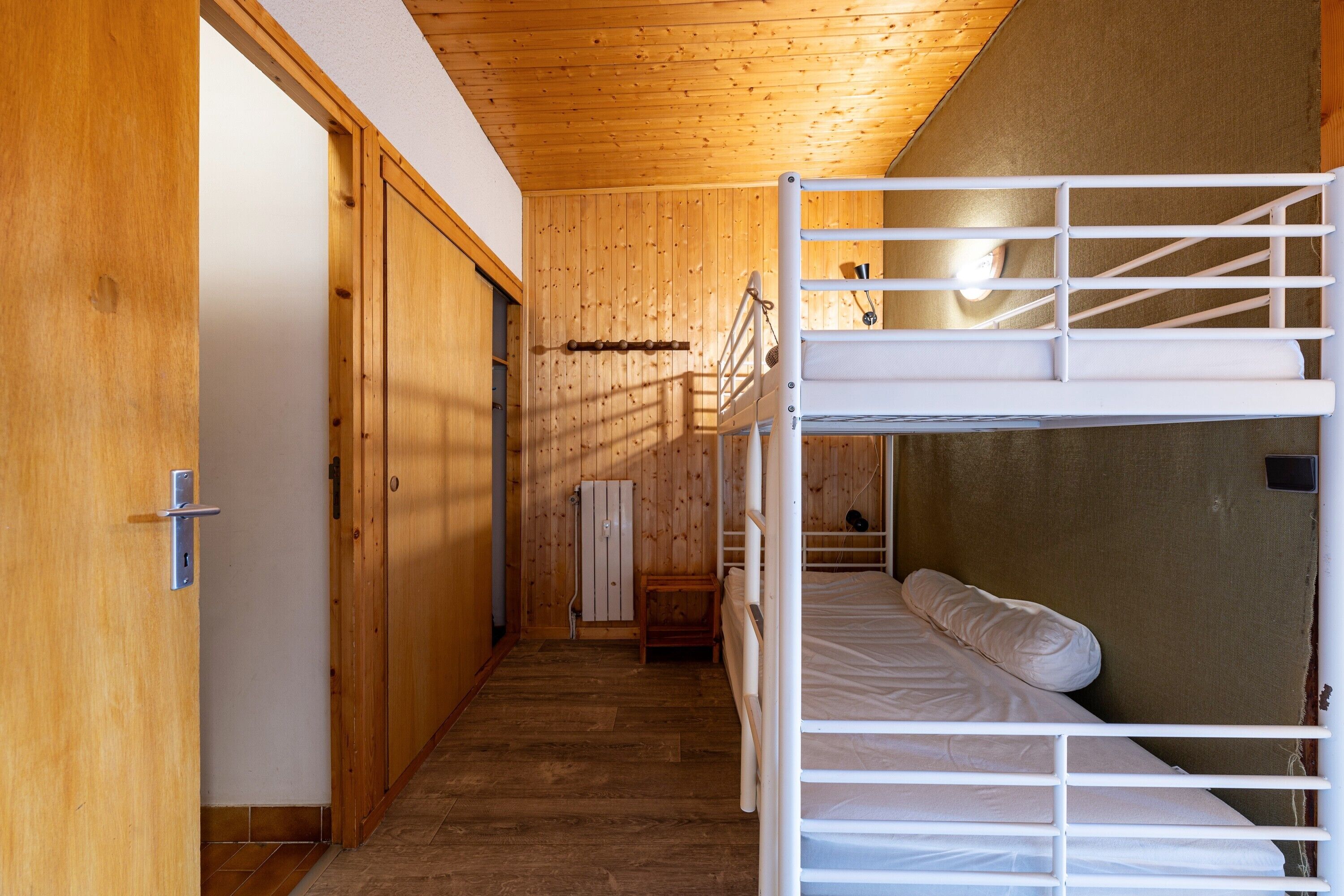 A bunk bed room with wooden walls, a door, and a radiator.