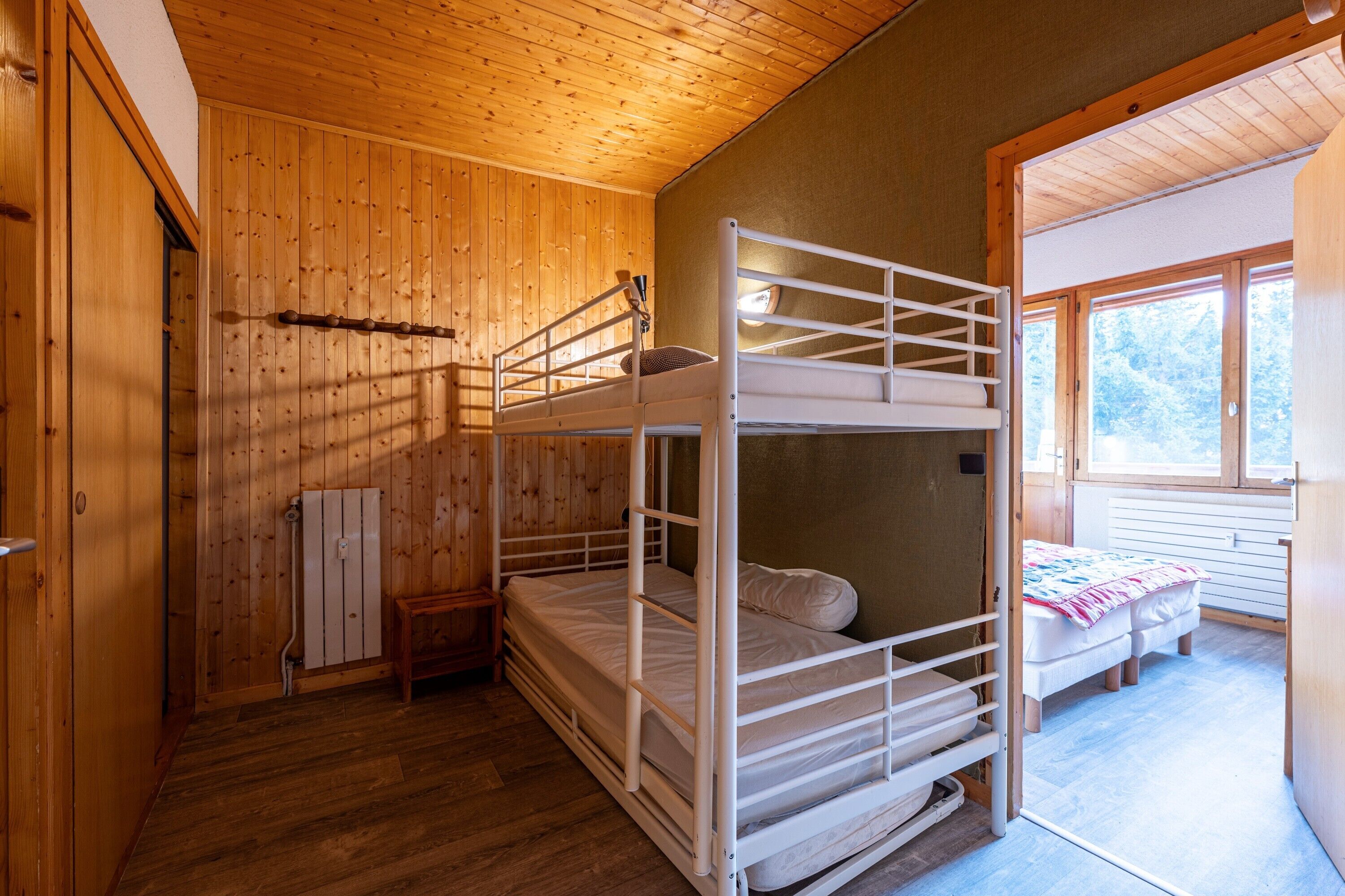 Ein Schlafraum mit Etagenbetten, Holzwänden, einem Heizkörper und einem Fenster.