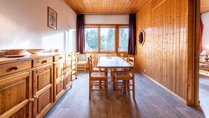 A wooden interior with a dining table and chairs, wooden cabinets, and a window with a view of trees. - Apartment 26 – 9 Guests with Mountain View and Balcony (Les Allues)
