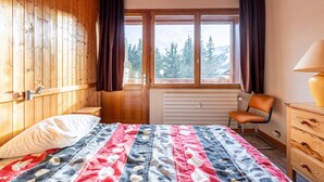 A wooden-paneled room with a bed, a chair, a dresser, and a window with a view of trees. - Apartment 26 – 9 Guests with Mountain View and Balcony (Les Allues)