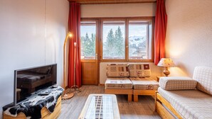 A cozy room with a television, sofa, and window with curtains. - Apartment 26 – 9 Guests with Mountain View and Balcony (Les Allues)