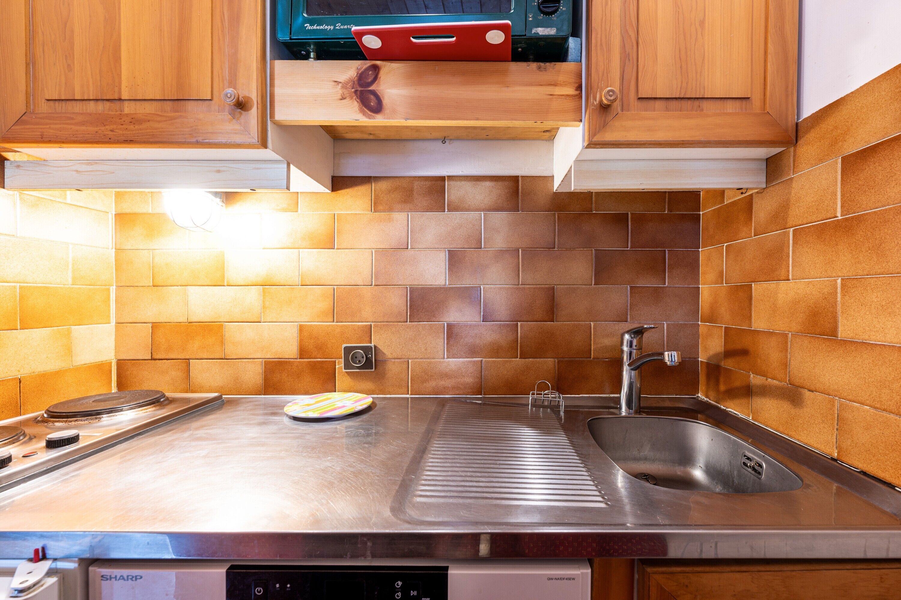 A kitchen with a stainless steel countertop, a sink, and wooden cabinets.