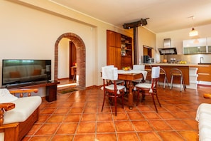 A living room with a TV, a dining table with chairs, a kitchen area with cabinets and a sink, and a tiled floor. - 'Villa Vittoria - Santa Tecla' with Sea View, Wi-Fi and Air Conditioning (Acireale)