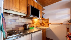 A compact kitchen with wooden cabinets, a built-in microwave, a dishwasher, and a tiled backsplash.