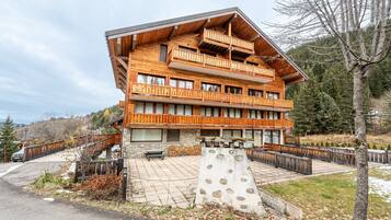 A multi-story wooden building with balconies, a stone facade, and a paved courtyard.
