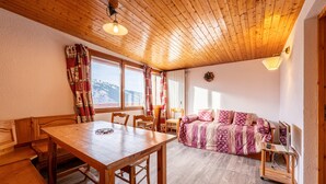 A wooden ceiling, a dining table with chairs, a sofa, a TV stand, and a window with curtains.