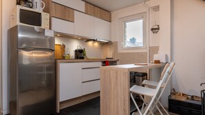 Una cocina moderna con un refrigerador de acero inoxidable, armarios de madera, un ventanal y un pequeño comedor.