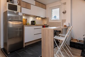 A modern kitchen with a stainless steel refrigerator, wooden cabinets, a window, and a small dining area.