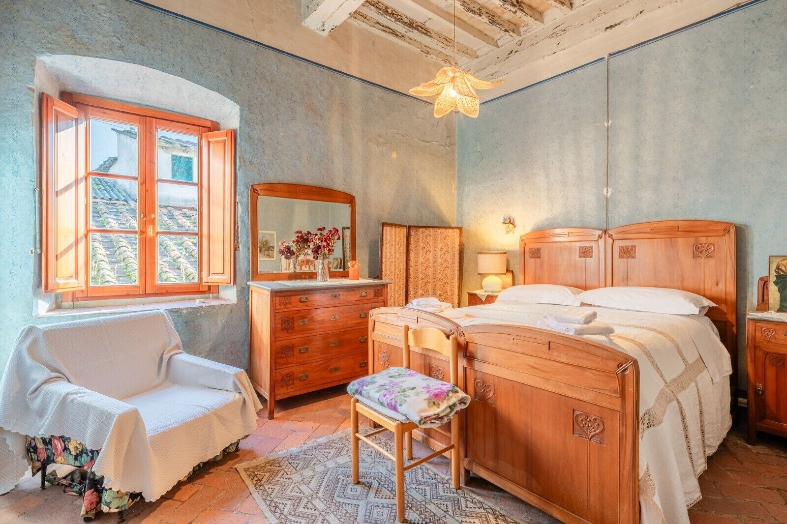 Una camera da letto con un letto in legno, una sedia, una cassettiera, uno specchio e una finestra con tende.