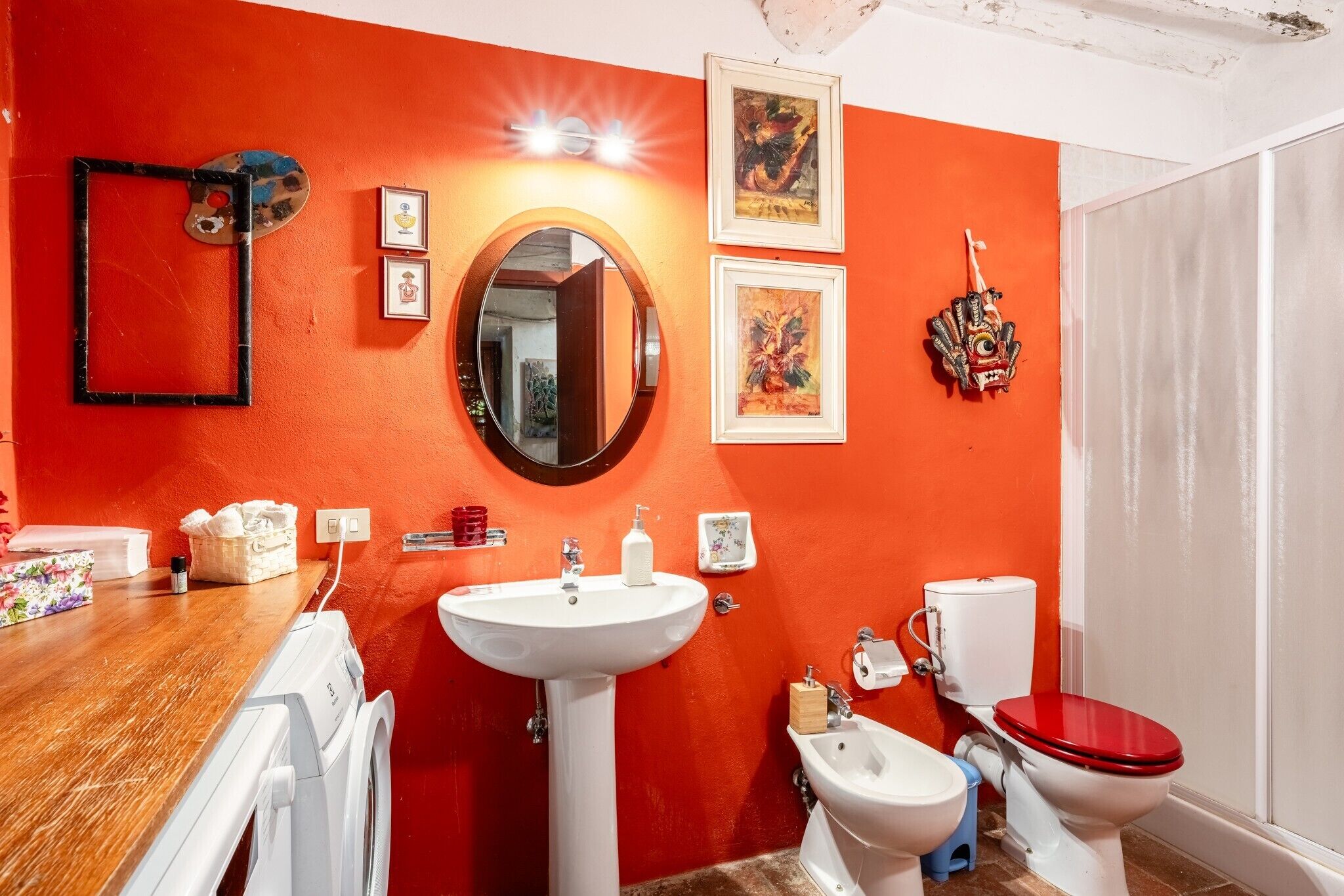 Un baño con una pared roja, un espejo redondo, un lavabo blanco, un inodoro y un bidé.
