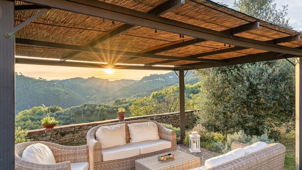 An outdoor seating area with wicker furniture and a stone wall backdrop. - Villa Gabriella with Beautiful Garden (Piazzano)