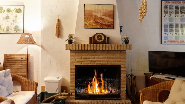 A living room with a fireplace, wicker furniture, a television, and wall art. - Room 'La Huerta' with Mountain View and Private Terrace (Hornos)