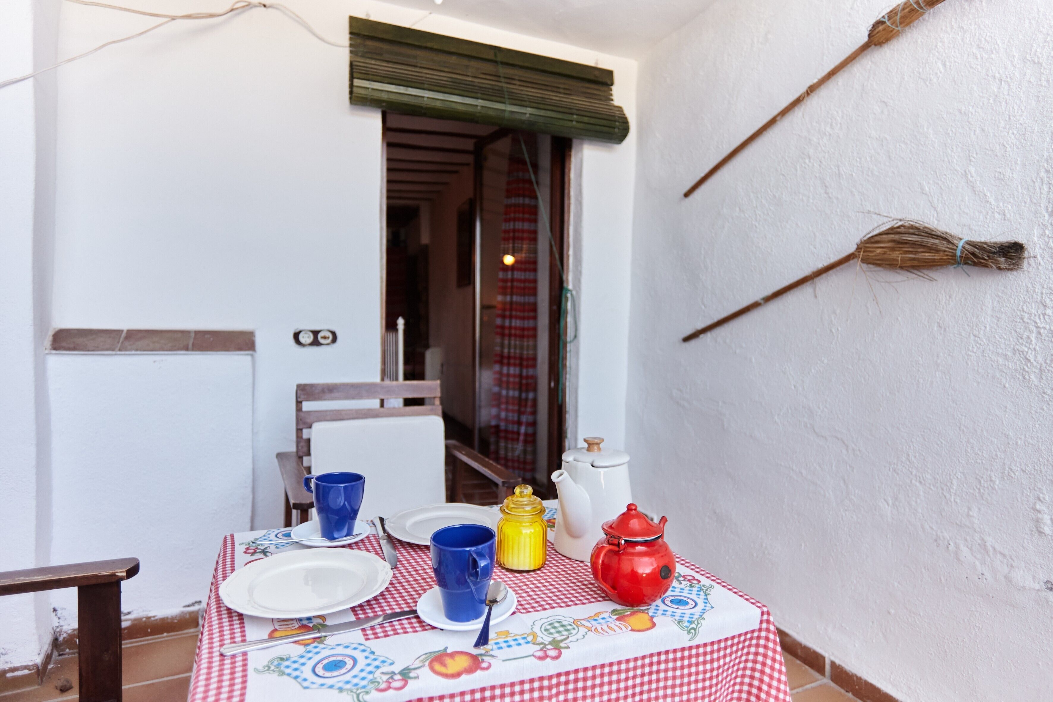 A dining table with a checkered tablecloth, white plates, blue and yellow cups, and a red teapot.
