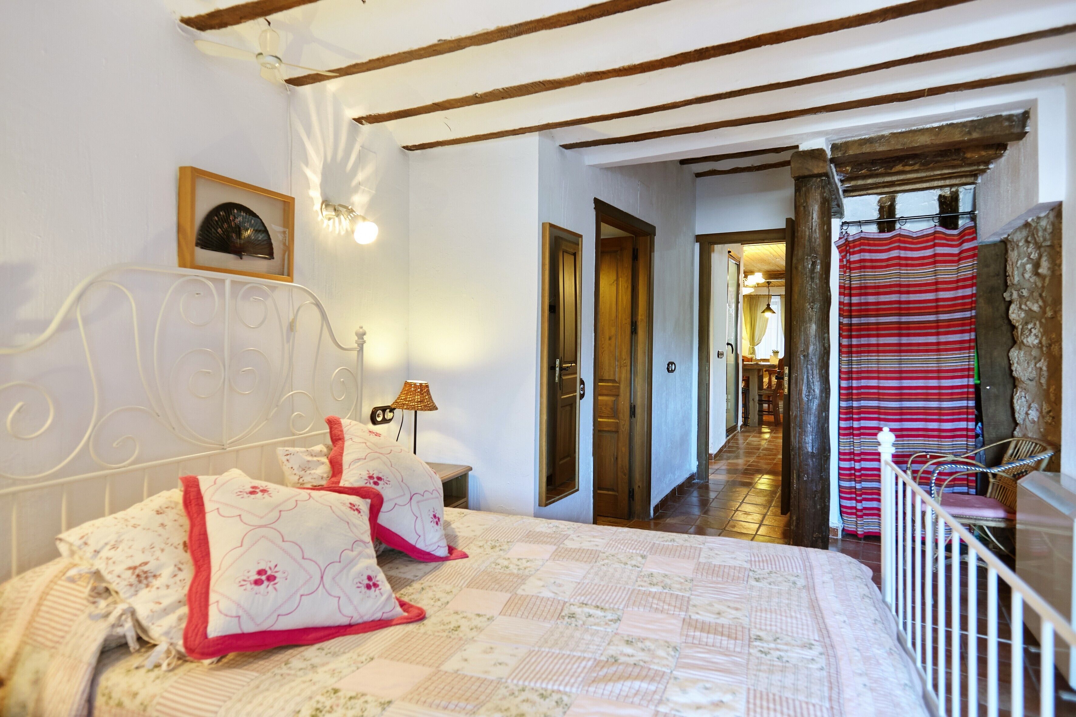 A bedroom with a bed, a bedside table, a lamp, a framed picture, and a door leading to another room.