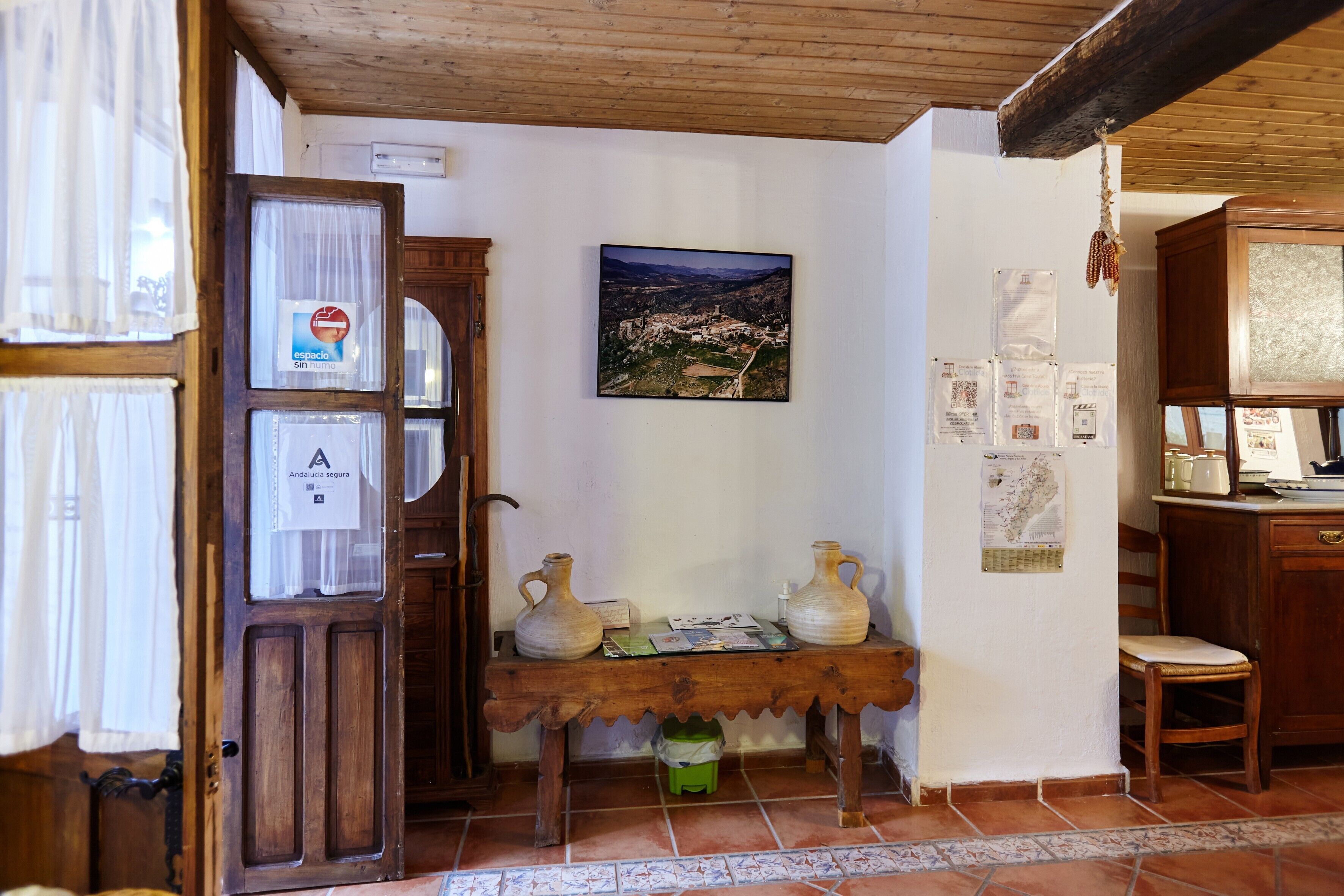 Un intérieur rustique avec une table en bois, deux pichets en céramique, une carte et une fenêtre avec des rideaux.