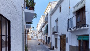 Una calle estrecha con edificios blancos, balcones y un perro acostado en el suelo.