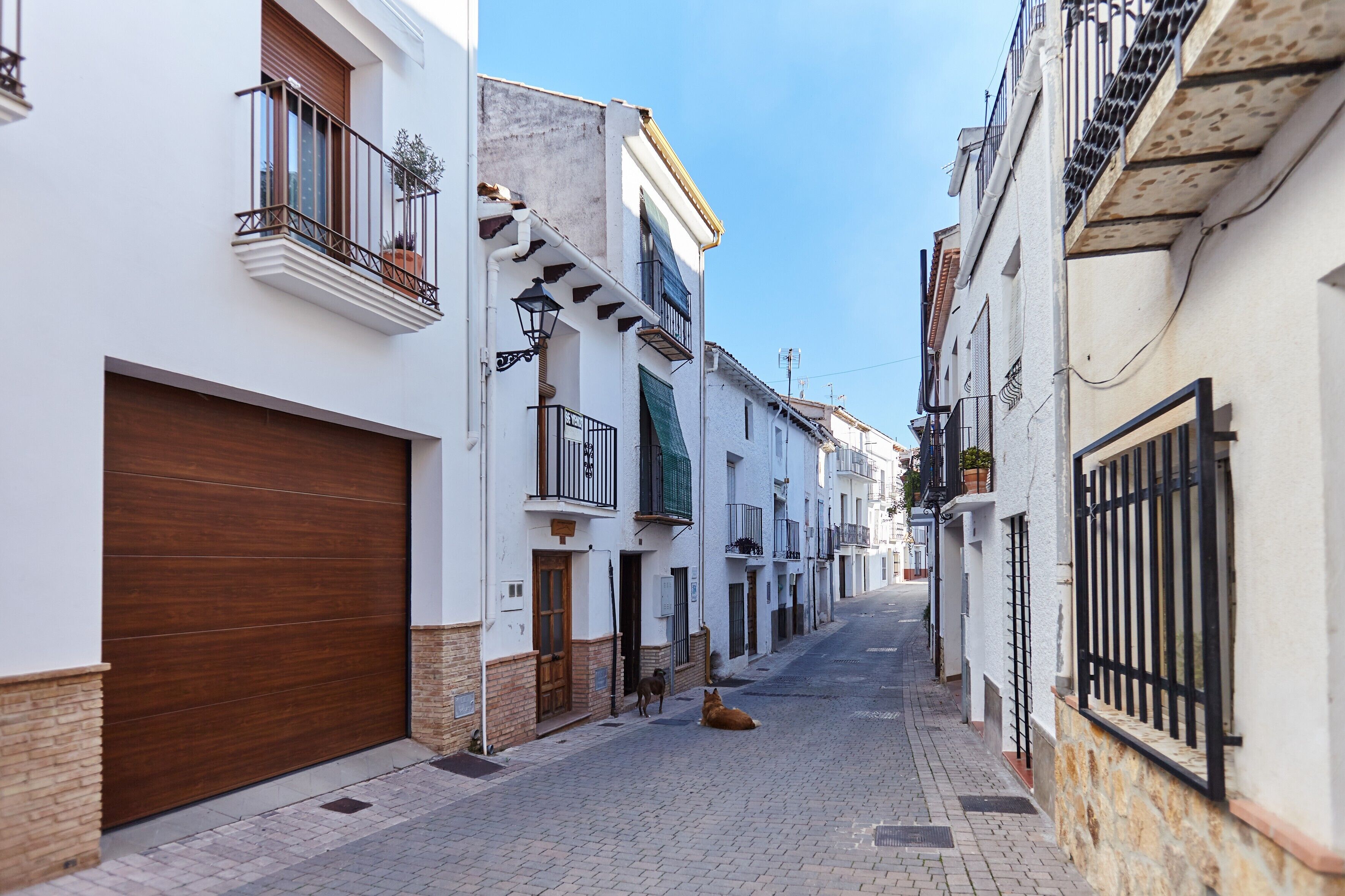 Una calle estrecha flanqueada por edificios, con balcones, una puerta de garaje de madera y un camino adoquinado.